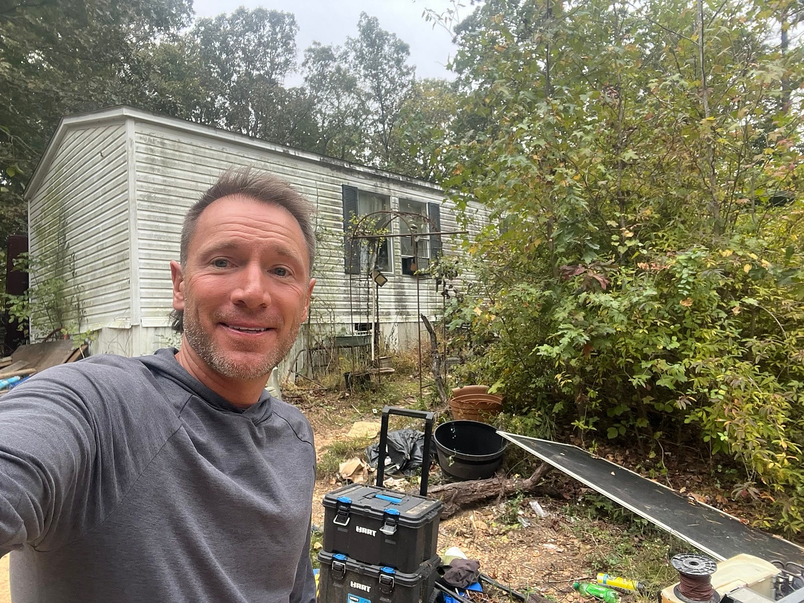 Rusty on a job site in front of a weathered mobile home he is buying as-is