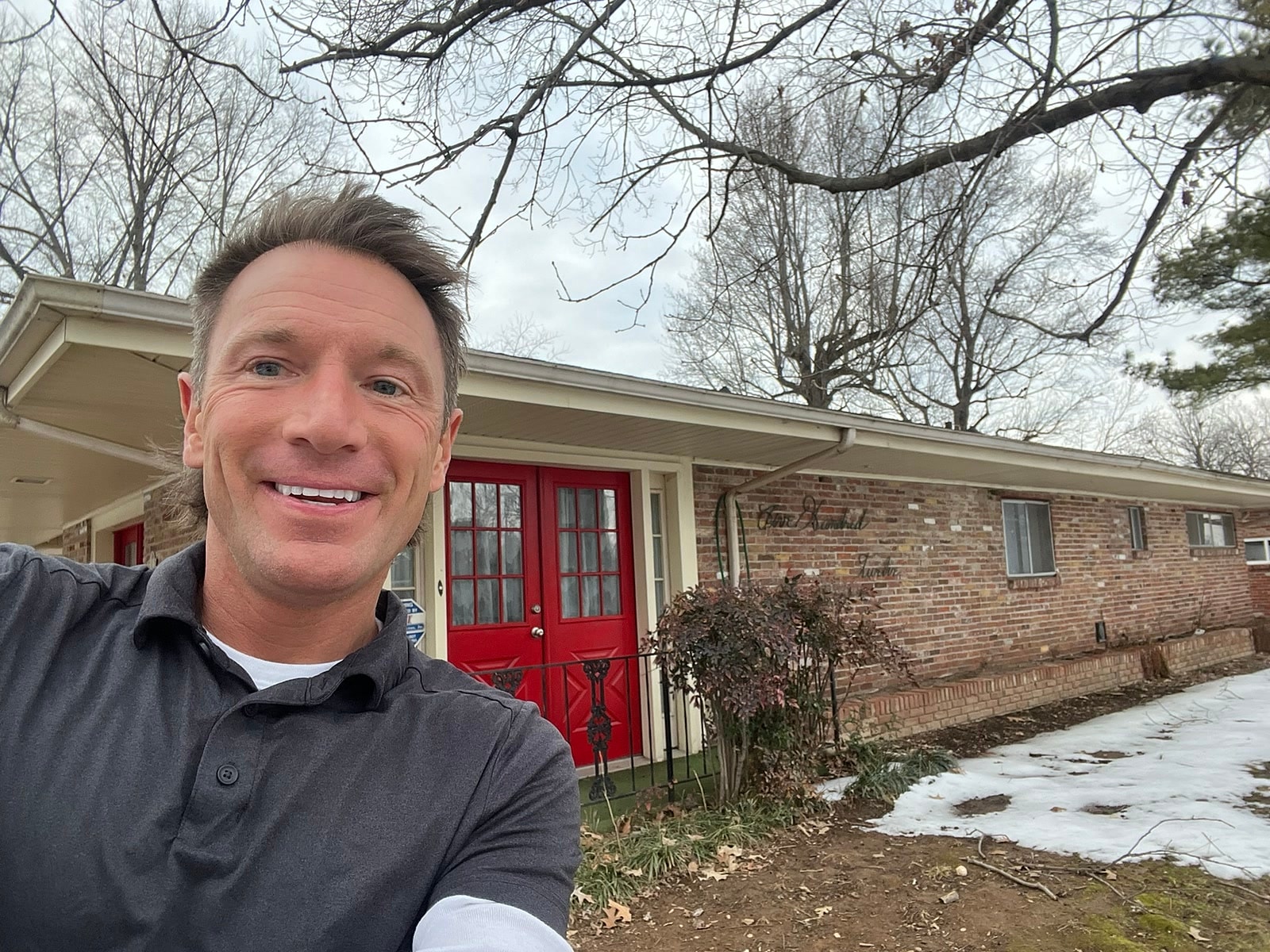 Rusty in front of a brick ranch with bright red double doors in Jonesboro, Arkansas